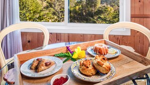 A dining table with plates of food and a tray, set against a window with a forest view. - Rendezvous Mendocino (Gualala)
