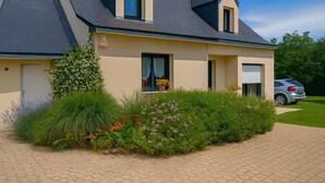 Ein modernes, zweistöckiges Haus mit Satteldach, Garage und einem gepflegten Garten mit verschiedenen Pflanzen und Blumen.