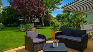 Ein Außenbereich mit Terrassenausstattung, Korbmöbeln, einem großen Blumentopf und einem Baum mit violetten Blättern.