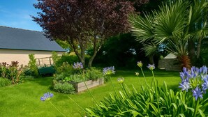 Ein gepflegter Garten mit Rasenfläche, blühenden Pflanzen und einem Gebäude mit Satteldach.