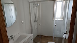 Un bany modern amb una cabina de dutxa de vidre, un lavabo blanc i un vàter.
