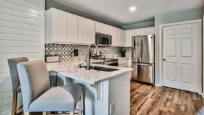 Una cocina moderna con armarios blancos, un refrigerador de acero inoxidable y un microondas integrado.