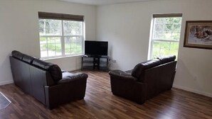 Ein Wohnzimmer mit zwei Ledersofas, einem Flachbildfernseher und großen Fenstern.