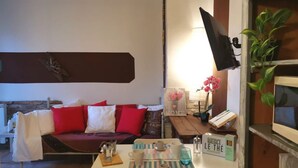 A cozy living room with a sofa, a coffee table with cups and a book, a wall-mounted TV, and a plant. - Bnbook-Appartamento Bilocale Il Geco (Olgiate Olona)