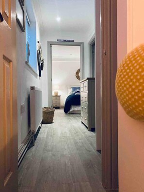A hallway leading to a bedroom with a bed, dresser, and a sign reading 'Captain's Quarters.' - Stylish Refurb Apartment with King & Bunk Cabin (St Ives)