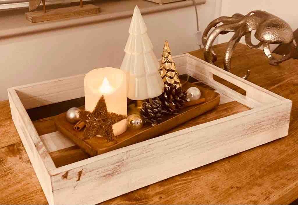 Ein hölzernes Tablett mit einer Kerze, Kiefernzapfen und einer Weihnachtsbaumkugel auf einem Tisch.
