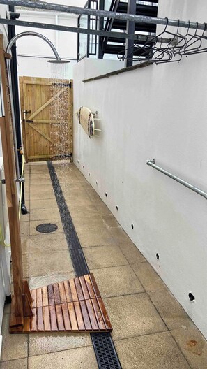 Un área de ducha con una puerta de madera, un estante metálico y un desagüe.