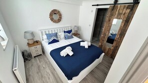 Un dormitorio con cama, mesitas de noche, espejo, radiador y una puerta de madera.