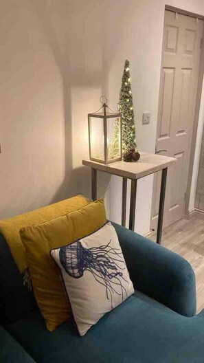 Una habitación con un sillón azul, una mesita con un árbol de Navidad y un farol, y una puerta blanca al fondo.