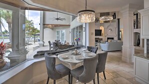 Un comedor espacioso con una gran mesa dispuesta para seis personas, rodeada de sillas cómodas. Un candelabro cuelga en lo alto, y un ventanal ofrece vistas del patio exterior.