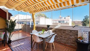 A covered patio with a table and chairs, a potted plant, and a view of buildings in the background. - Cosy Urban Penthouse In The Heart Of Fuengirola (FUENGIROLA)