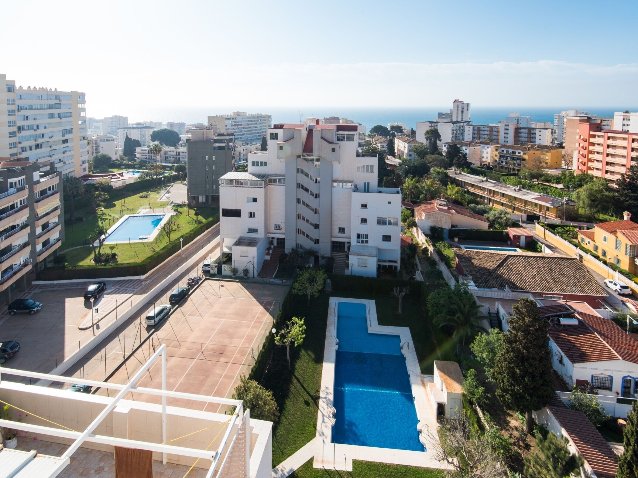 Um hotel alto com piscina, várias varandas e vista para a cidade e o mar.