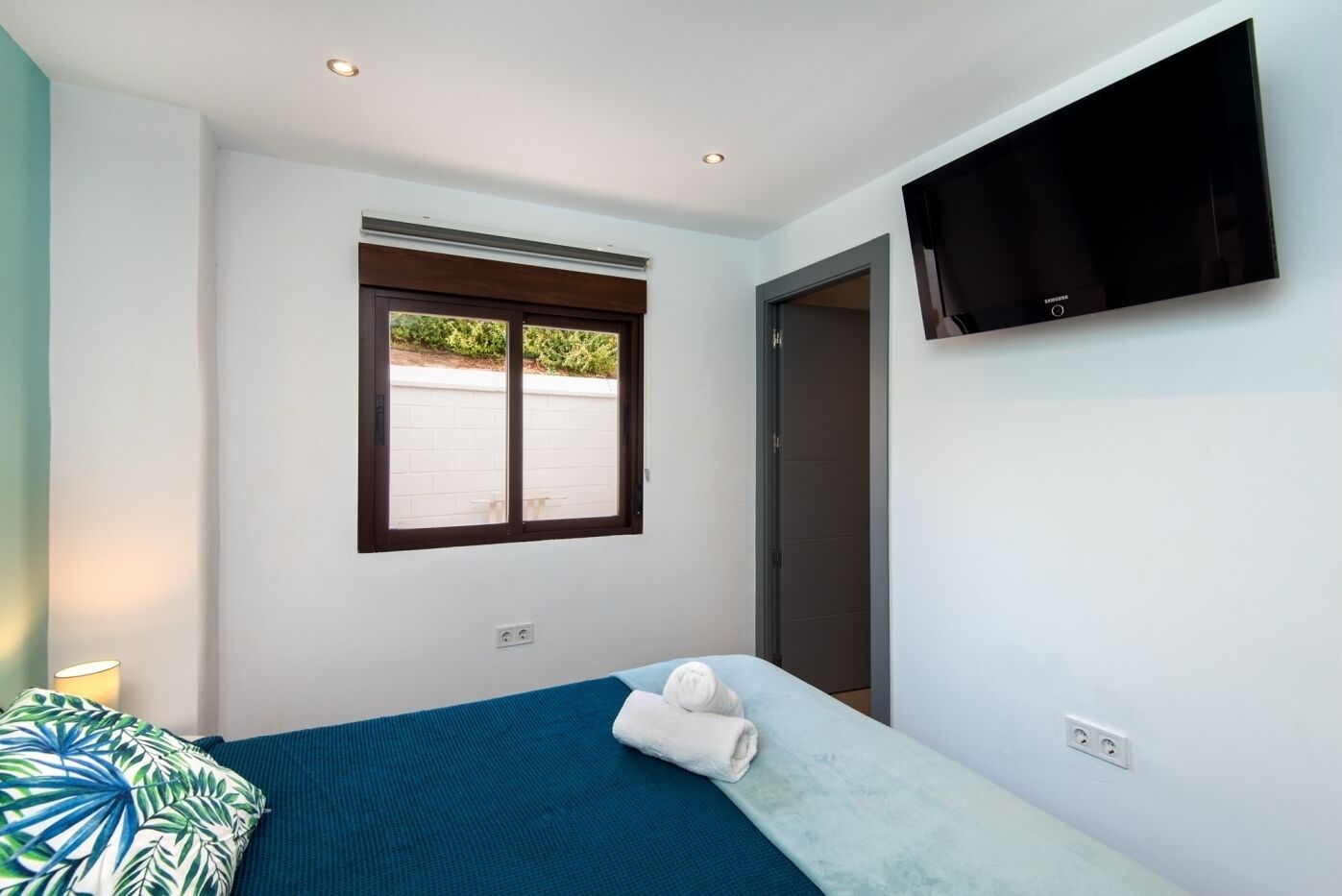 A bedroom with a bed, a window, a TV, and a door.