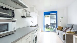 Eine moderne Küche mit Einbauofen, Mikrowelle und Waschmaschine. Ein Essbereich mit grauem Sofa und Tisch ist ebenfalls vorhanden.