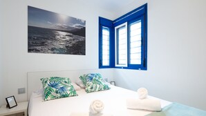 Ein Schlafzimmer mit einem Bett, Kissen, einem gerahmten Bild und einem Fenster mit blauen Lamellen.