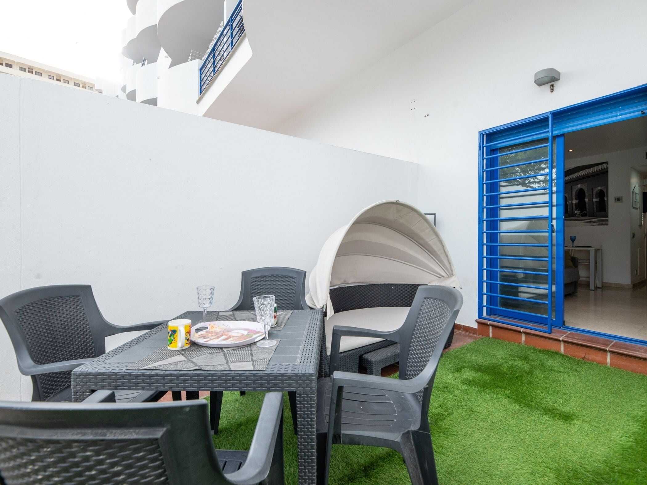 Eine Terrasse mit Tisch und Stühlen, ein überdachter Sitzbereich und eine blaue Tür zu einem Innenraum.