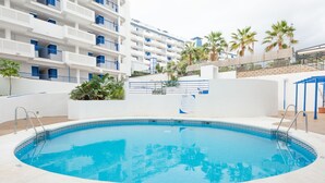 Ein Schwimmbecken in Weiß und Blau, umgeben von einem weißen Gebäude mit Balkonen und Palmen.