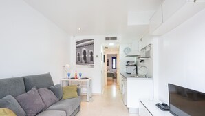Eine moderne Wohnung mit grauem Sofa, Fernseher, einer Küche mit weißen Schränken und einem Essbereich mit Tisch und Stühlen.