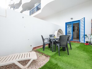 Un patio con tavolo e sedie, un piccolo giardino con erba sintetica e una porta blu che dà su un ambiente interno.