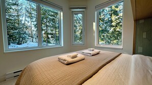 Un dormitorio con una cama grande, dos ventanas y vistas a árboles cubiertos de nieve.
