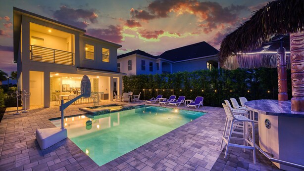 A modern outdoor pool area with lounge chairs and a bar, surrounded by houses and a clear sky. - Golden Bear Oasis | 6 Bed, 5.5 Bath Villa, Private Pool, Game Room, Themed Kids' Rooms (Kissimmee)