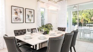 A dining area with a white table set for six, black upholstered chairs, and two framed abstract paintings on the wall. - Golden Bear Oasis | 6 Bed, 5.5 Bath Villa, Private Pool, Game Room, Themed Kids' Rooms (Kissimmee)