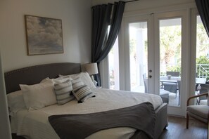 A bedroom with a large bed, a nightstand, a lamp, and a view of the outdoor patio. - Ocean Hammock Paradise-5BR 4BA, Private Pool, 1 Min walk to Beach,Family Retreat (Palm Coast)