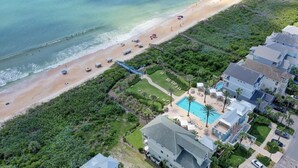 Luftaufnahme eines Küstengrundstücks mit Strand, Schwimmbad und Wohngebiet.