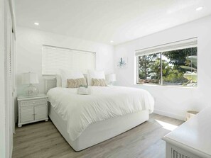 Camera da letto moderna con un letto grande, un comodino, una finestra vista verde e arredamento bianco.
