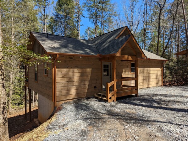Situated in a forested area, this cabin features a pitched roof and a front porch with stairs leading to the entrance.