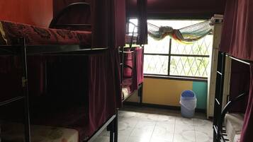 Un dormitorio con literas, una ventana con vistas a zonas verdes, una mesita pequeña y un cubo de basura.