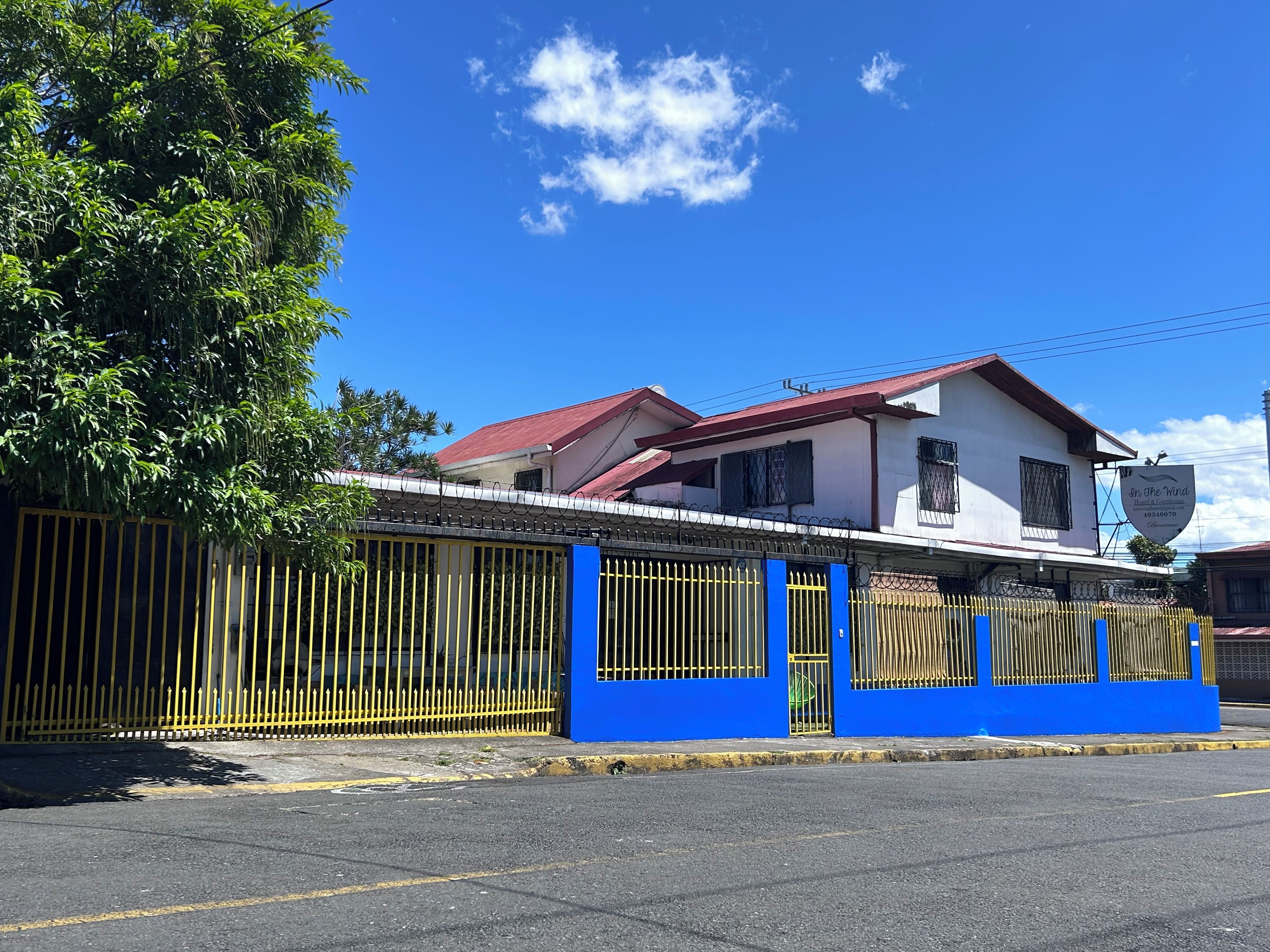 A two-story building with a red roof and white walls, surrounded by a blue and yellow fence.