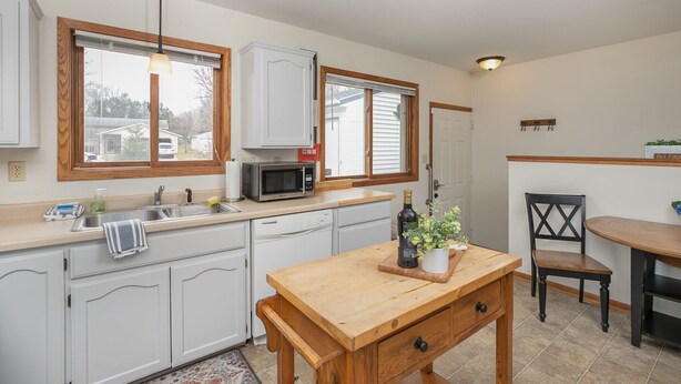 A kitchen with white cabinets, a microwave, a wooden table, and a chair. - Are you traveling to Rochester? Be our guest!!  (Rochester)