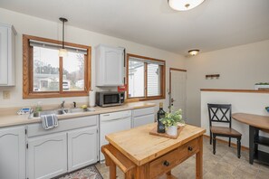 A kitchen with white cabinets, a microwave, a wooden table, and a chair. - Are you traveling to Rochester? Be our guest!!  (Rochester)