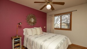 A bedroom with a bed, a ceiling fan, a window, a bookshelf, and a mirror on the wall. - Are you traveling to Rochester? Be our guest!!  (Rochester)