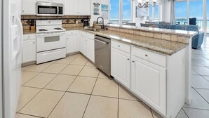 A modern kitchen with white cabinets, a granite countertop, stainless steel appliances, and a view of the city through large windows. - Hidden Treasure -3BR Sleeps 8 (Navarre Beach)