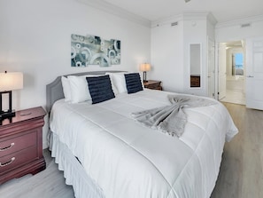 A neatly arranged bedroom with a large bed, a bedside table with a lamp, a dresser, and a wall-mounted abstract painting. - Hidden Treasure -3BR Sleeps 8 (Navarre Beach)