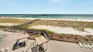 A beach view with a wooden deck, lounge chairs, and a pool area. - Hidden Treasure -3BR Sleeps 8 (Navarre Beach)