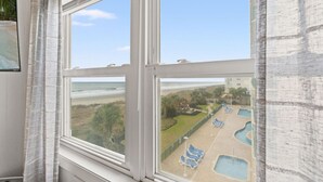 Une fenêtre donnant sur une piscine et une plage.