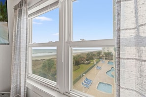 Une fenêtre donnant sur une piscine et une plage.