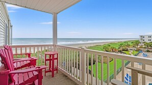 Un balcon donnant sur la plage, des fauteuils Adirondack rouges et une balustrade blanche.