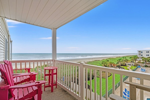 Un balcon donnant sur la plage, des fauteuils Adirondack rouges et une balustrade blanche.