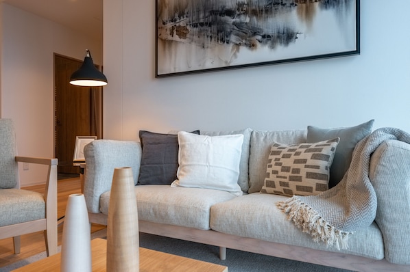 A modern living room with a grey sofa, a wooden coffee table, and a black pendant lamp.