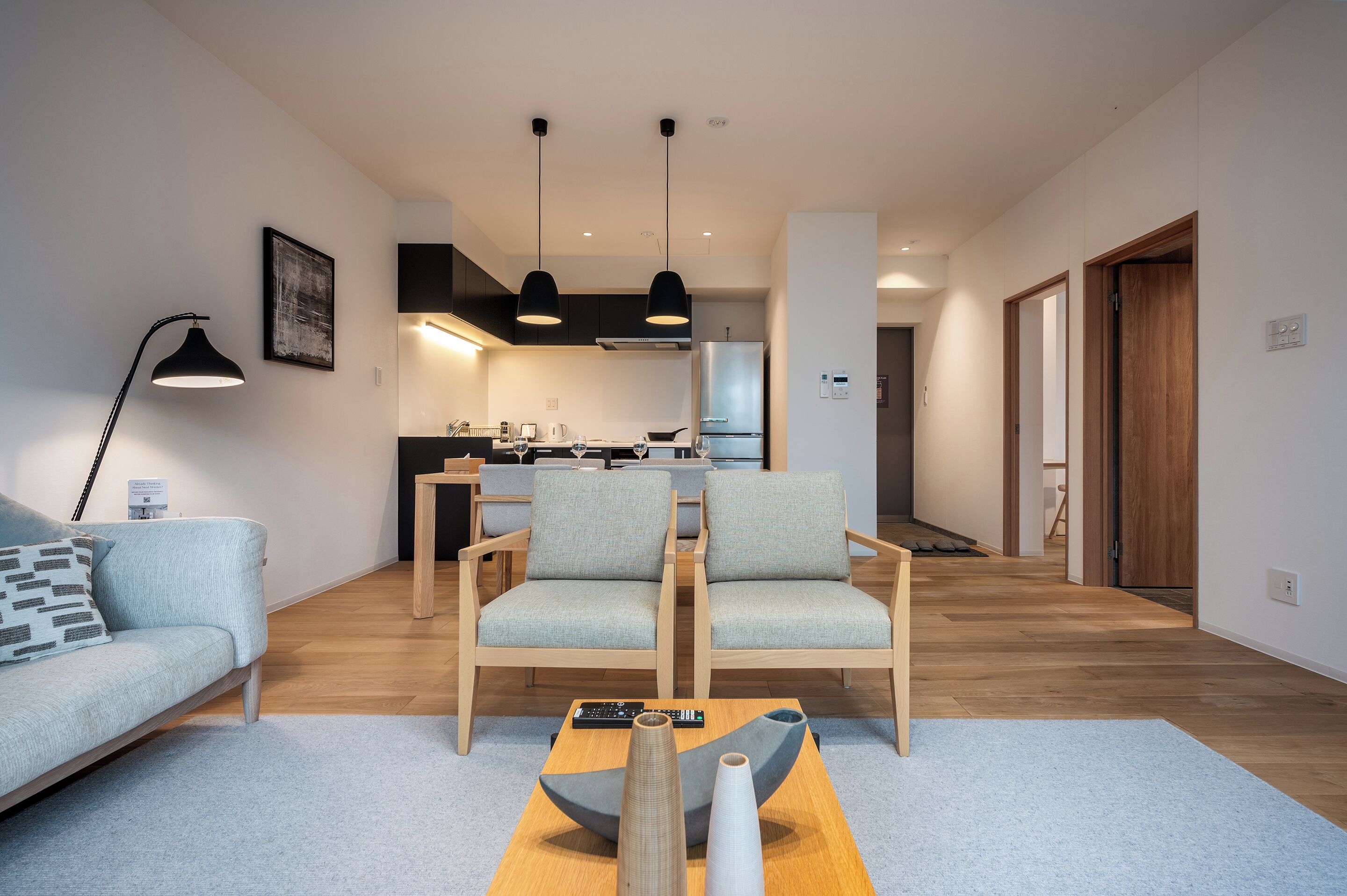 A modern living room with a sofa, two armchairs, a coffee table, and a kitchen in the background.