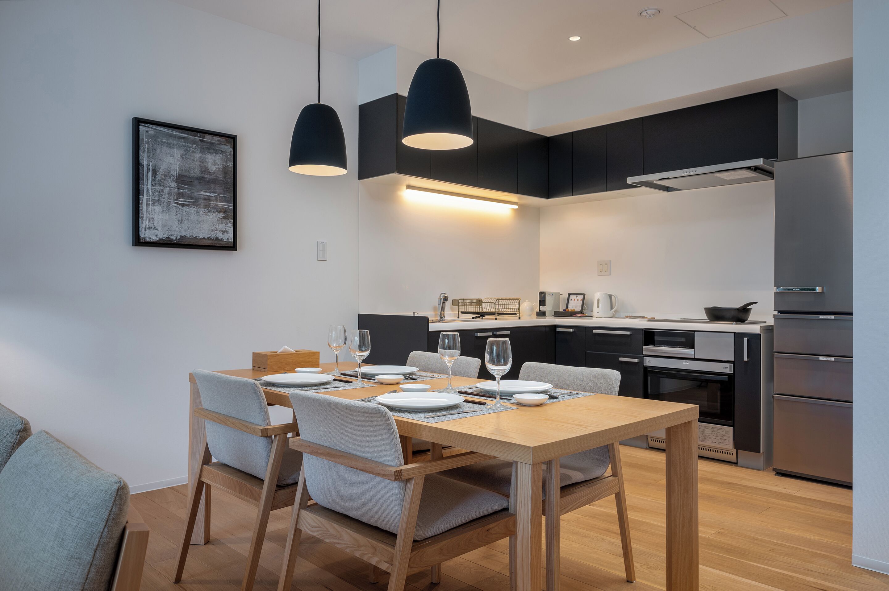 Eine moderne Küche mit dunklen Schränken, einem Edelstahlkühlschrank und einem Essbereich mit Holztisch und Stühlen.