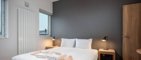A modern bedroom with a large bed, bedside lamps, and a view through the window.