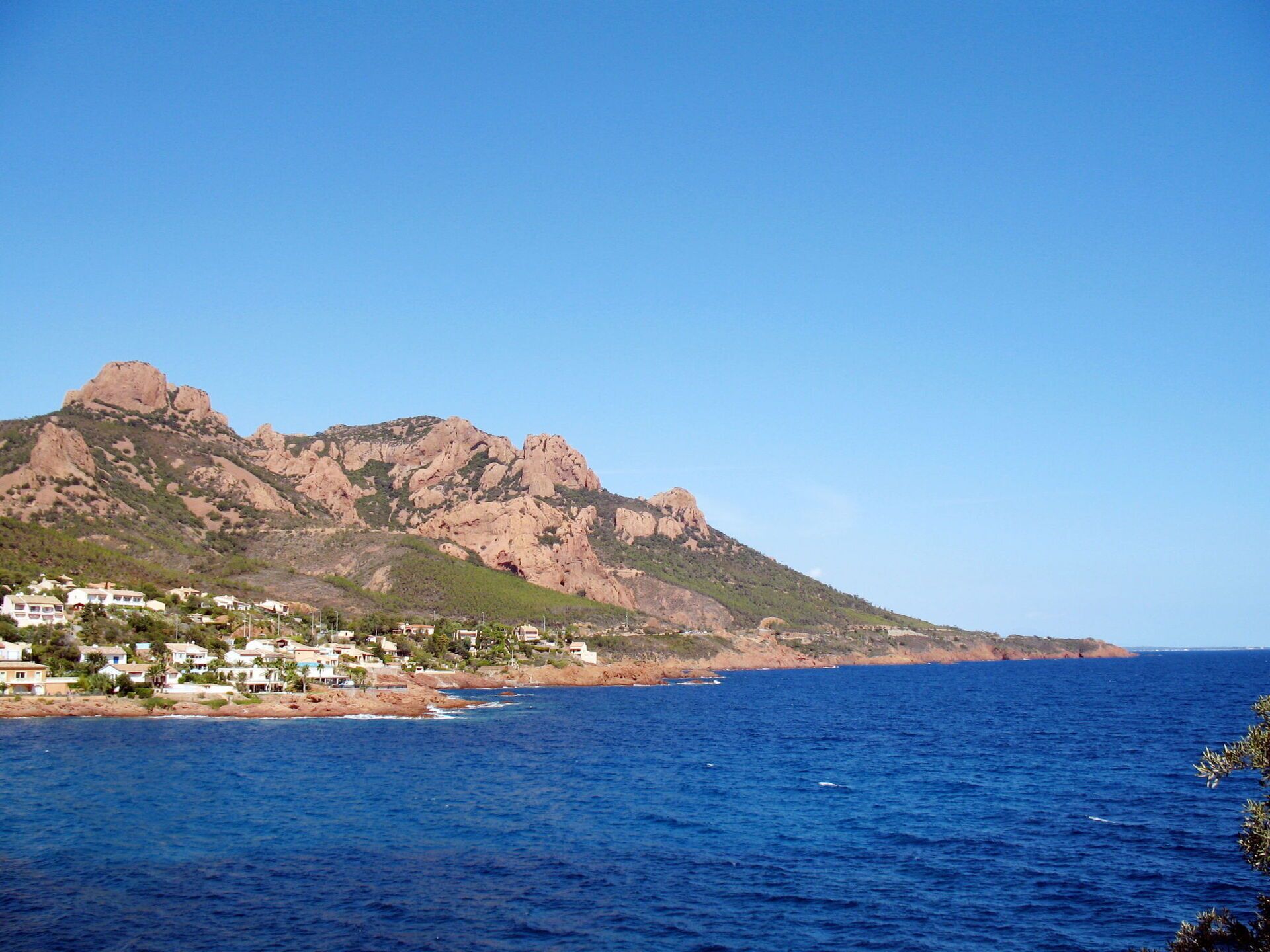 Une ville côtière avec des maisons le long du littoral, une montagne rocheuse en arrière-plan et une mer bleue et limpide.