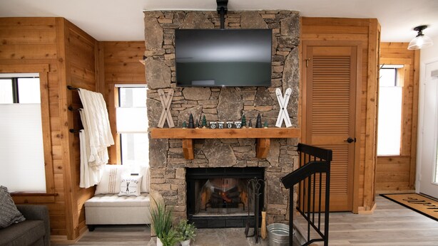 A cozy living room with a stone fireplace, a mounted TV, and wooden walls. - Mountain Adventures with heated pool near Pittsburgh, State Parks, Falling Water (Champion)