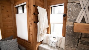 A cozy cabin interior with wooden walls, a bench with pillows, and a window with a towel hanging on the wall. - Mountain Adventures with heated pool near Pittsburgh, State Parks, Falling Water (Champion)