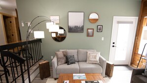 A living room with a wooden staircase, a grey sofa, a coffee table with magazines, and a large mirror on the wall. - Mountain Adventures with heated pool near Pittsburgh, State Parks, Falling Water (Champion)